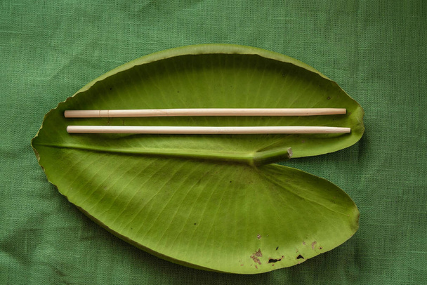 Lotus leaf as a plate. Organic disposable tableware. Wooden chopsticks. Linen green tablecloth. Ecology concept. Copy space. - Fotoğraf, Görsel
