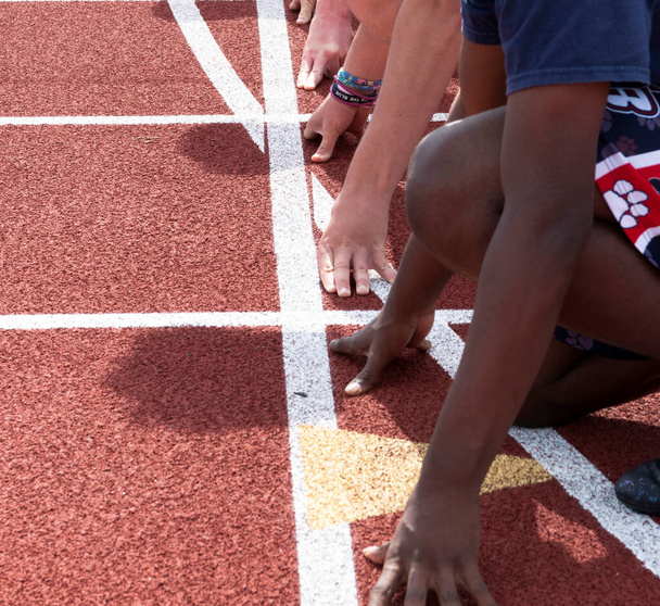 Pohled shora na ruce a paže středoškolských kluků připravených k zahájení sprintového závodu na závodní dráze. - Fotografie, Obrázek