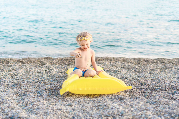 Lindo niño divertido jugando con colchón de natación amarillo en la orilla del mar. Vacaciones de verano en la playa, estilo de vida infantil, concepto de escena de playa. - Foto, Imagen