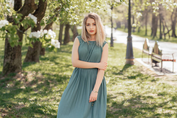 Beautiful blonde woman in a green long dress stays in a spring blooming garden. - Fotografie, Obrázek
