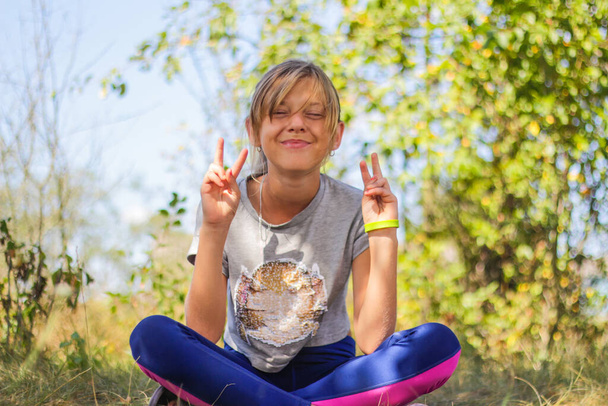 Defocus kaukasischen preteen Mädchen praktiziert Yoga im Park, Wald, im Freien, draußen. Spaß haben, Hupen zeigen. Wellness gesunder Lebensstil. Porträt eines Yoga-Mädchens. Grüner Hintergrund. Unscharf. - Foto, Bild