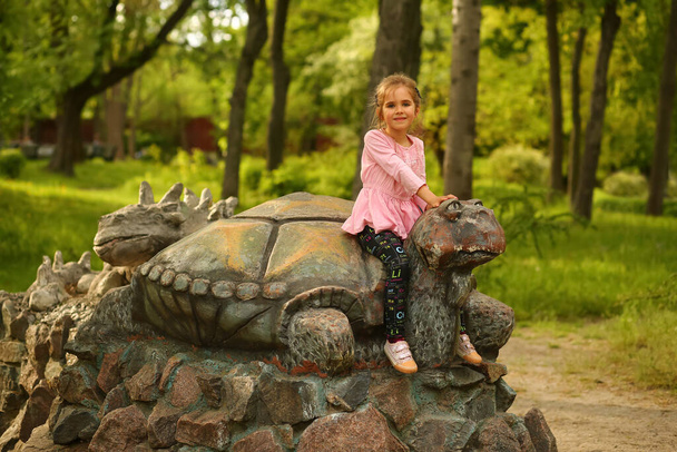 Retrato de una niña de cinco años sentada sobre una tortuga en el parque infantil - Foto, imagen