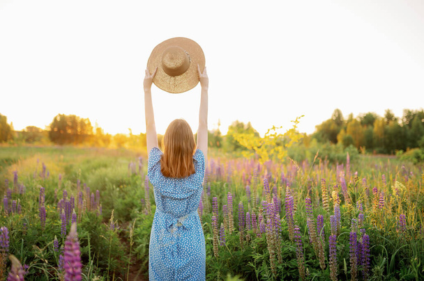 Kobieta trzyma kapelusz w rękach na polu i patrzy na zachód słońca. Widok z tyłu - Zdjęcie, obraz
