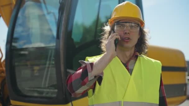 Excavator operator in hard hat talking by smartphone. - Footage, Video