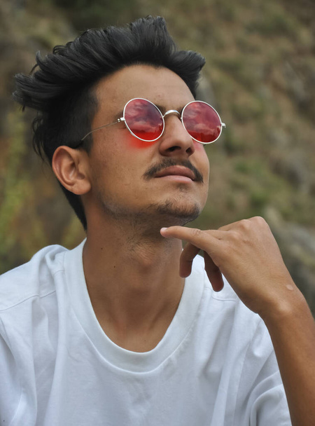 Closeup shot of a joyful young guy posing outdoor with looking up, A guy with wearing white t-shirt and red sunglasses  - Photo, Image