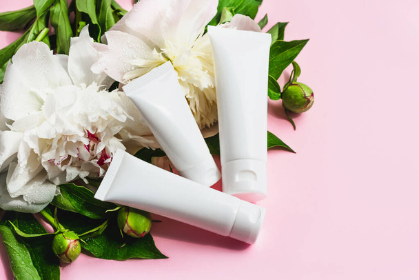 White cosmetic tubes mockup on pink background. Beauty branding cream container with peony flowers. - Foto, Bild