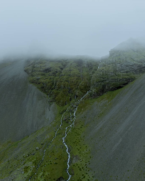 Aerial drone view of beautiful nature dramatic landscape in Iceland. Low clouds, fog on the mountains. Cold toned filter - 写真・画像