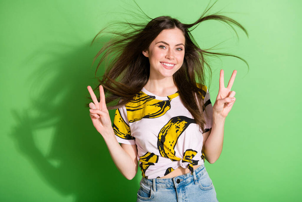 Photo of happy cool cheerful lady make v-signs hello fly hair smile good mood isolated on green color background - Foto, Imagen