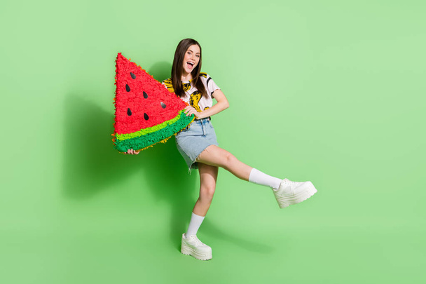 Full length photo of cheerful happy pretty young woman hold big watermelon slice isolated on green color background - Foto, afbeelding