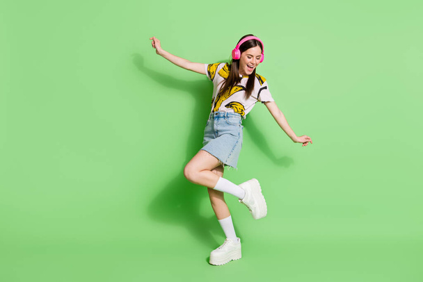 Full body photo of attractive young positive woman listen music dance isolated on green color background - Foto, immagini
