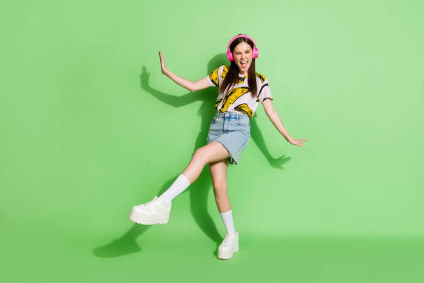 Foto de tamaño completo de la joven excitada chica sonriente funky en los auriculares escuchar música bailando aislado sobre fondo de color verde - Foto, Imagen