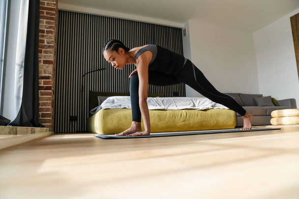 Attractive young healthy african woman doing yoga exercises on a fitness mat in the bedroom, yoga positions - Photo, image