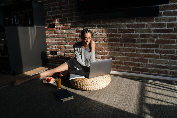 Focused african american girl in earphones working with laptop at home - Foto, afbeelding