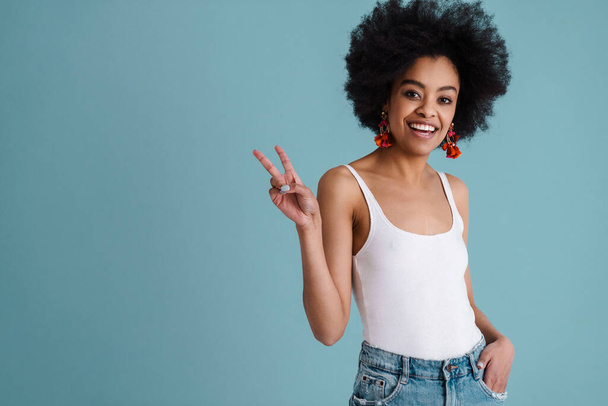 Happy african american girl smiling and showing peace sign at camera isolated over blue background - Фото, зображення
