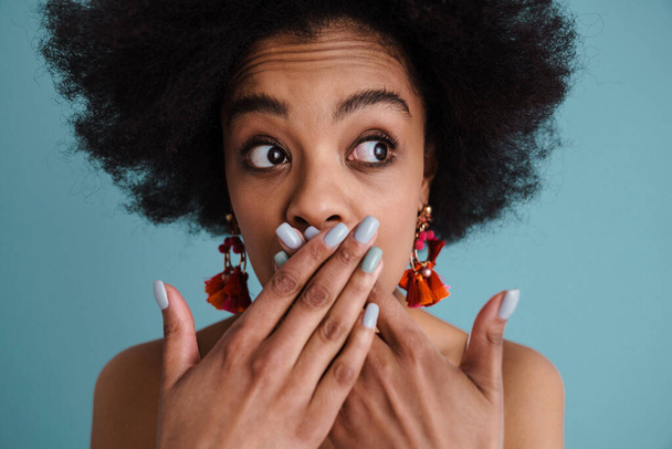 Portrait of a afro american shocked woman covering mouth isolated on a blue background - Фото, зображення