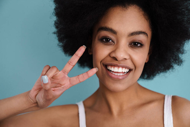 Close up of a cheerful young attractive woman grimacing isolated over blue background, peace gesture - Foto, Imagen