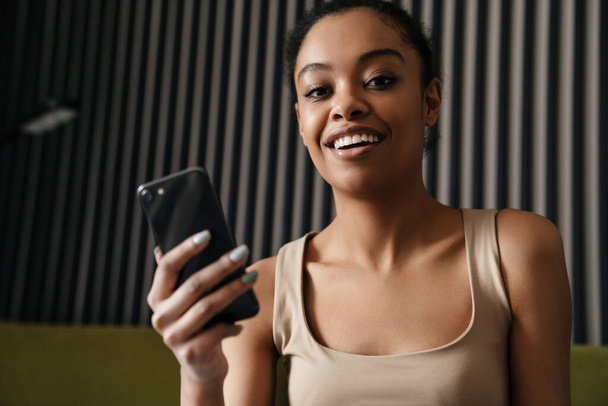 Happy african american girl smiling while using mobile phone at home - Фото, зображення