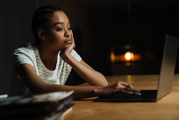 Black tired woman working with laptop while sitting at table in office - Foto, imagen