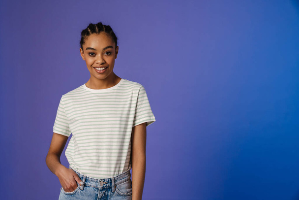 Young black woman in t-shirt smiling and looking at camera isolated over blue background - Фото, зображення