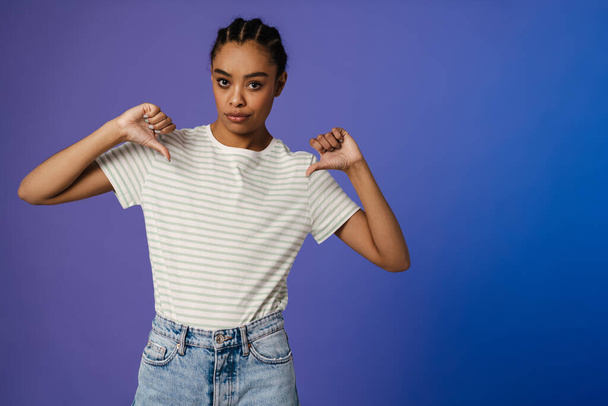 Young black woman in t-shirt pointing fingers at herself isolated over blue background - 写真・画像