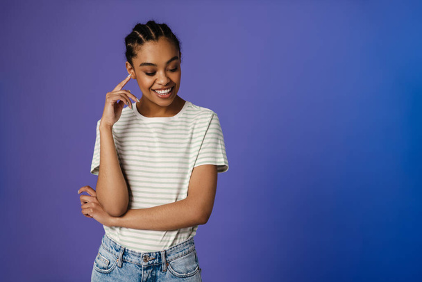 Young black woman in t-shirt smiling and looking downward isolated over blue background - Photo, image