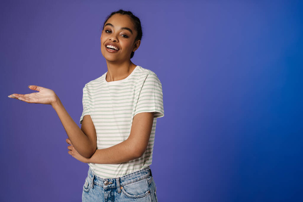 Young black woman in t-shirt smiling and holding copyspace isolated over blue background - Zdjęcie, obraz