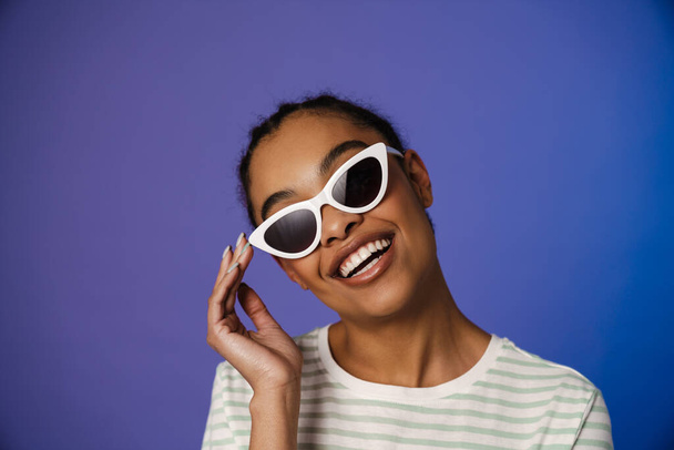 Young black woman in sunglasses smiling at camera isolated over blue background - Fotografie, Obrázek