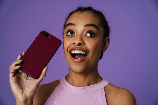 Young black woman smiling and holding mobile phone isolated over purple background - Foto, immagini