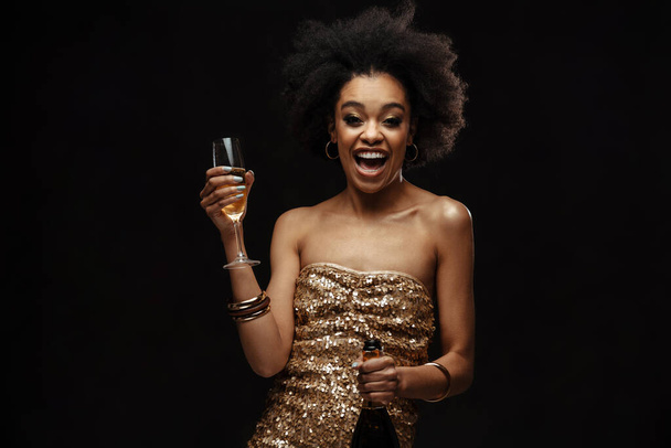 Excited african american woman in party dress drinking champagne isolated over black background - Foto, Imagem