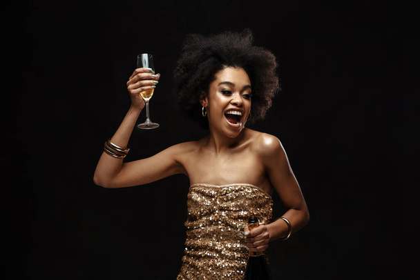Excited african american woman in party dress drinking champagne isolated over black background - Foto, afbeelding
