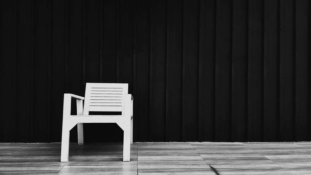 木製の椅子は、背景と右側のコピースペースのための黒いシャッター壁と茶色のタイルの床に置きます。モノクロームトーンでダークステンレス製の壁紙と席を取るためのオブジェクト. - 写真・画像