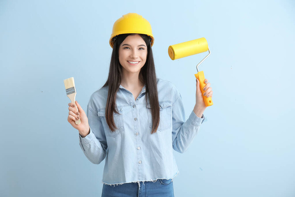 Young woman with brush and paint roller on color background - Foto, imagen