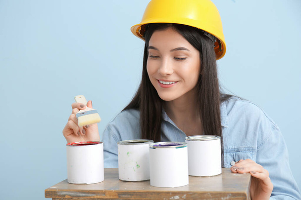 Young woman with brush and cans of paint on color background - Photo, Image