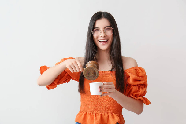 Schöne junge Frau mit Kaffeekanne und Tasse auf hellem Hintergrund - Foto, Bild