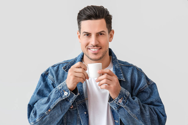 Knappe jongeman drinken koffie op lichte achtergrond - Foto, afbeelding