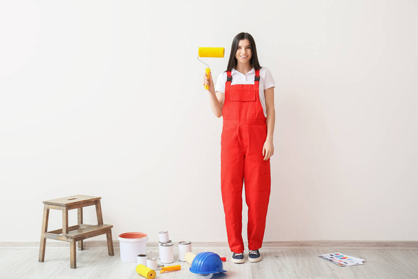 Młoda kobieta z wałkami lakierniczymi i puszkami lakieru przy ścianie - Zdjęcie, obraz