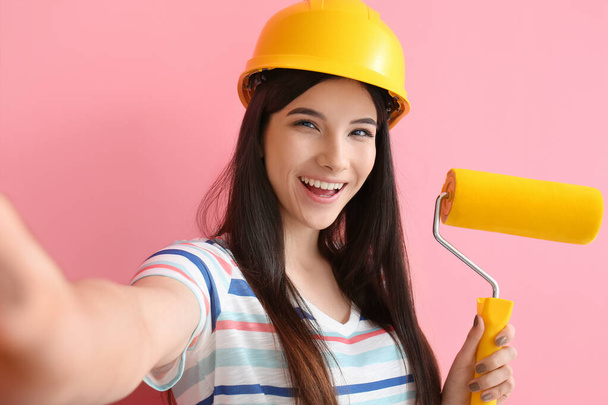 Young woman with paint roller taking selfie on color background - Photo, Image