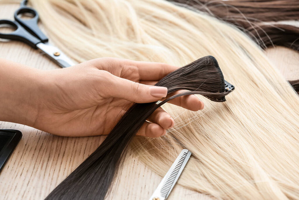 Female hairdresser with strand of brunette hair in beauty salon, closeup - Photo, Image