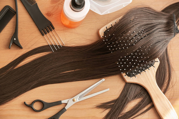 Прядь каштановых волос с ножницами и щетками на столе - Фото, изображение