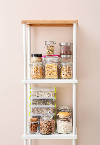 Jars and containers with different products on shelves near color wall - Photo, Image
