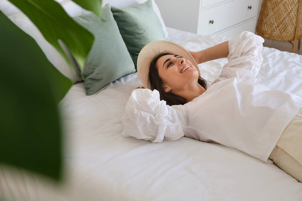 Jovem mulher em chapéu elegante deitado na cama no quarto - Foto, Imagem