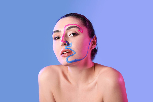 Beautiful young woman with paint on her face against color background - Fotó, kép