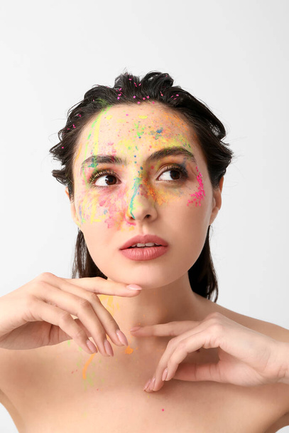 Beautiful young woman with paint on her face against light background - Photo, Image