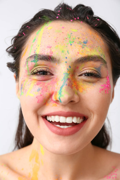 Mooie jonge vrouw met verf op haar gezicht tegen lichte achtergrond - Foto, afbeelding