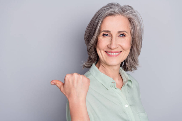 Photo of happy smiling beautiful mature woman point thumb copyspace advertisement isolated on grey color background - Zdjęcie, obraz