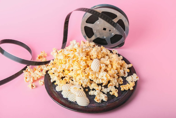 Plate with tasty popcorn and film reel on color background - Photo, Image