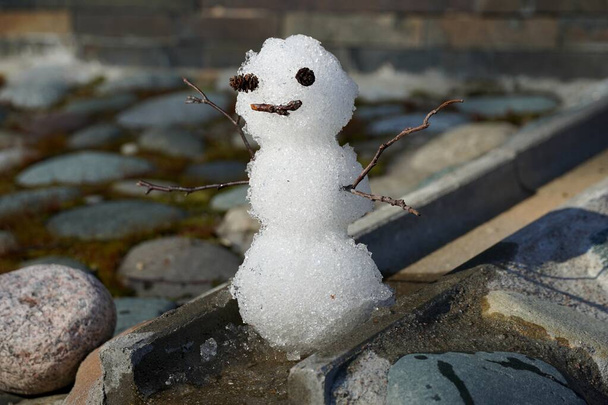 Close up Kleine grappige sneeuwpop in het voorjaar. Op de waterafvoer bestrating steen. - Foto, afbeelding