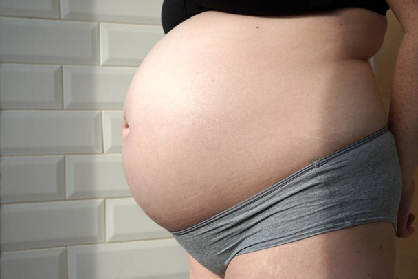 nagi duży brzuch ciężarnej kobiety. Dziewiąty miesiąc ciąży. stanik majtki - Zdjęcie, obraz