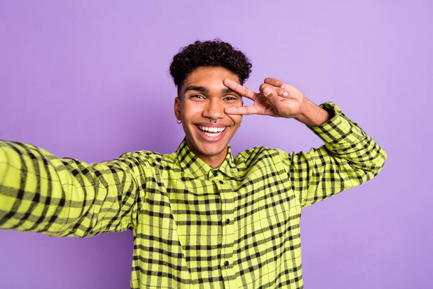 Photo portrait of guy showing v-sign gesture like taking selfie in plaid shirt isolated on pastel purple color background - 写真・画像