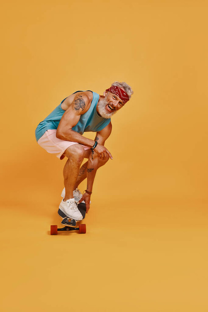 Full length of active senior man skateboarding against orange background - Foto, Imagem